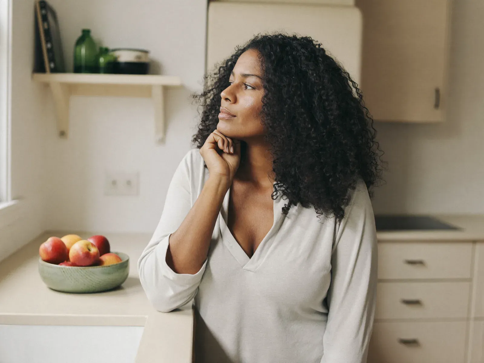 A woman in her kitchen looking out of the window, calm and thoughtful