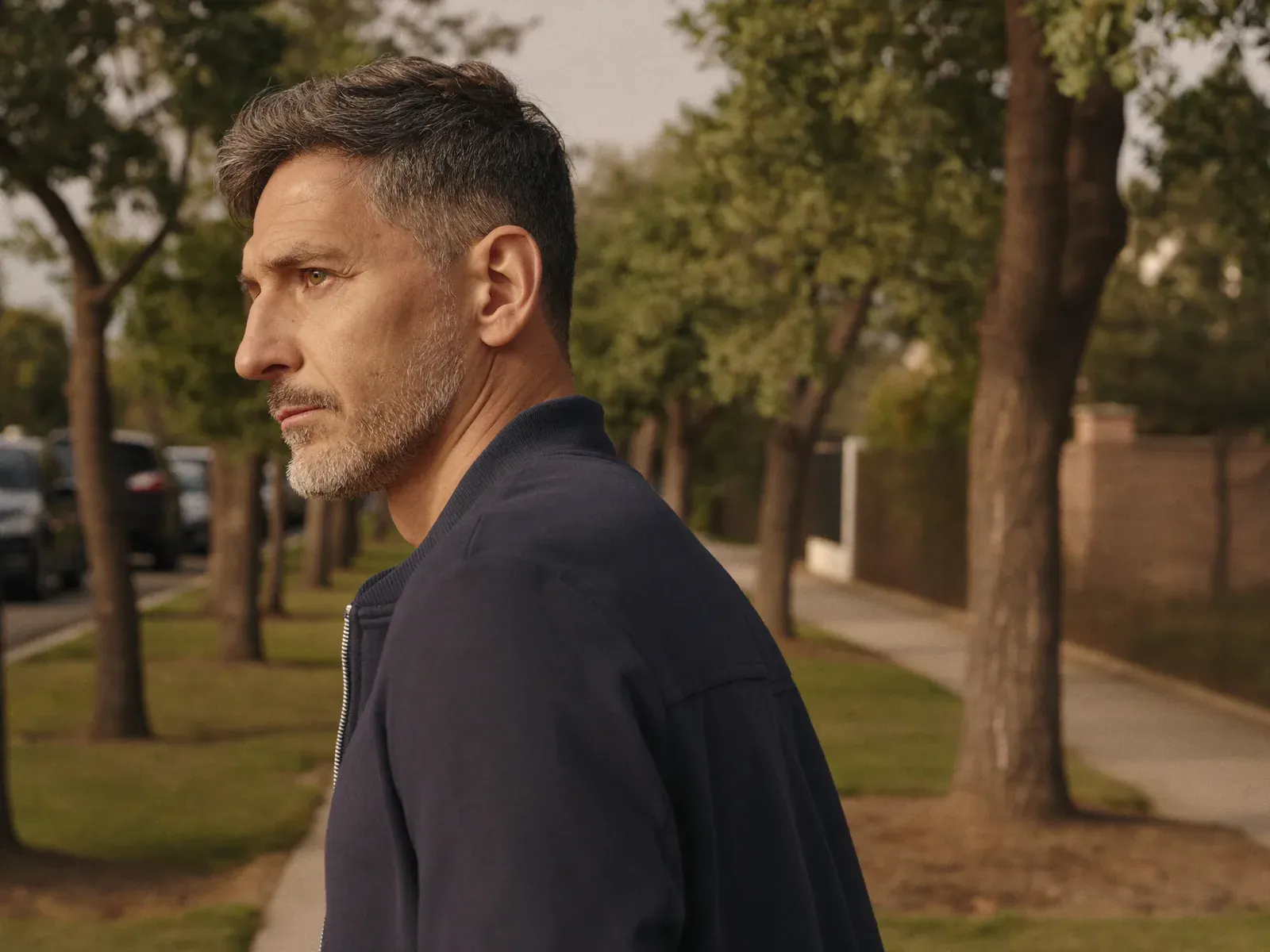 A man with a gray beard on a morning walk along a tree-lined street